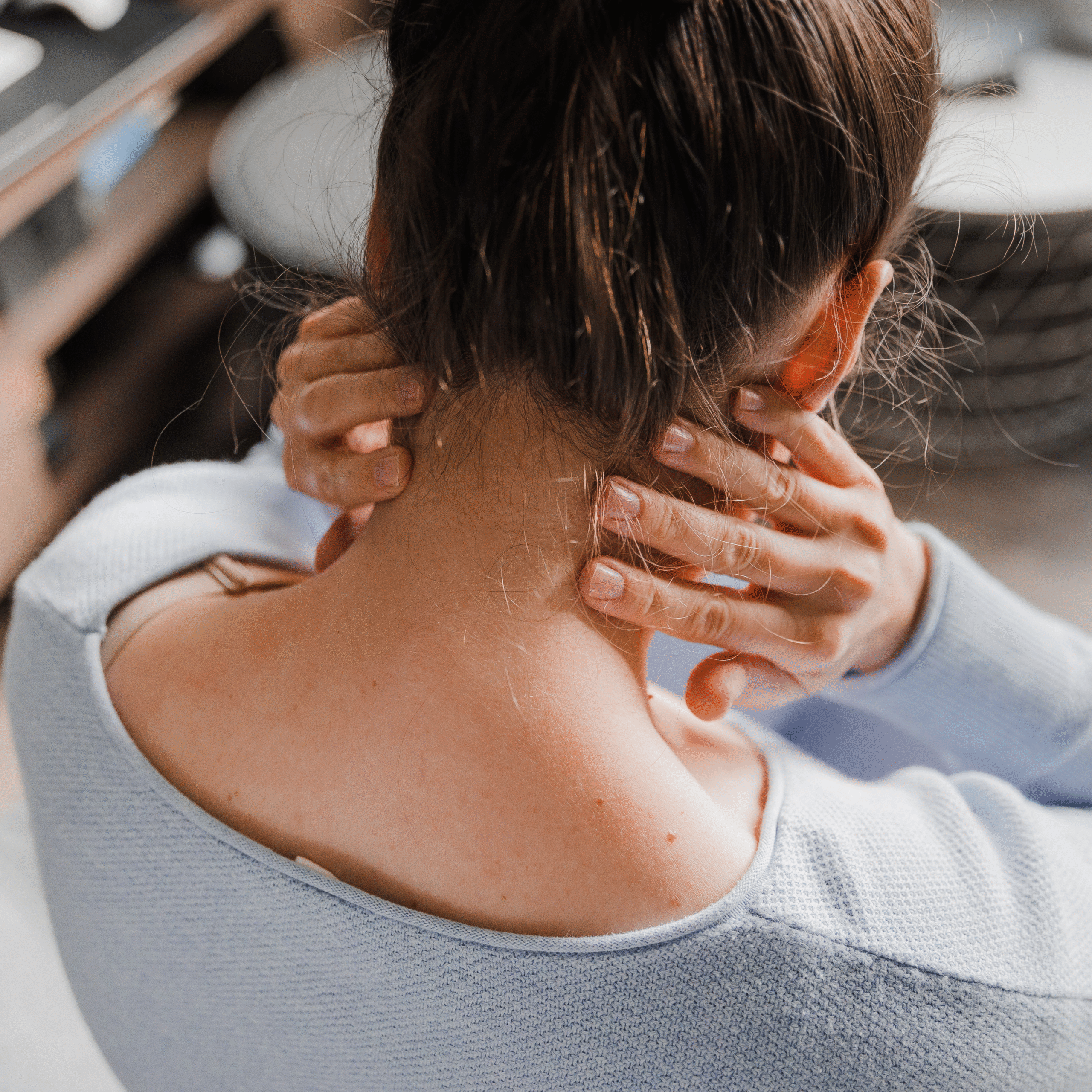 Vrouw met opgestoken haar die haar nek vasthoudt en zichtbaar last heeft van nekpijn door whiplash.